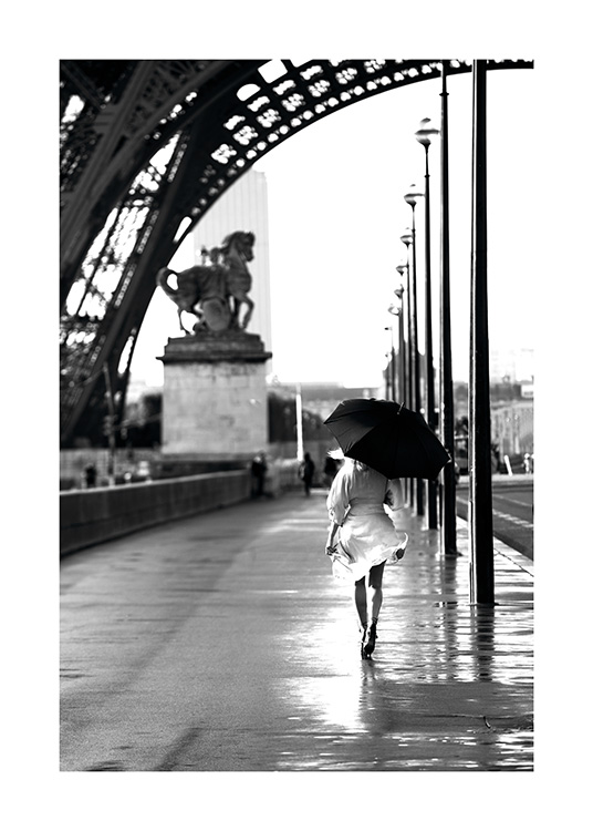  – Zwart wit foto van een vrouw die met een paraplu onder de Eiffeltoren loopt