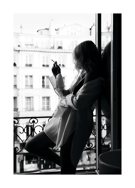  – Zwart wit foto van een vrouw in een oversized overhemd die een sigaret rookt voor een raam