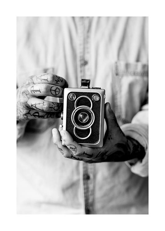  – Zwart wit foto van een ouderwetse camera, vastgehouden door een man met getatoeëerde handen