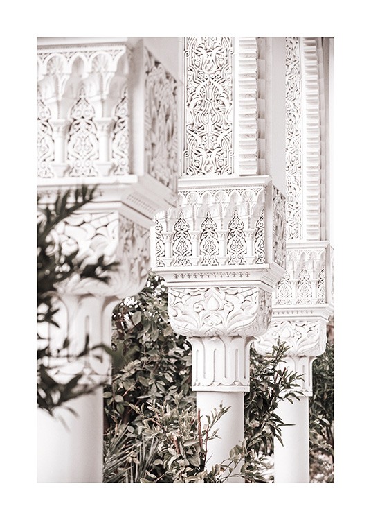 Close-upfoto van bewerkte witte pilaren met patronen en groene bladeren op de achtergrond