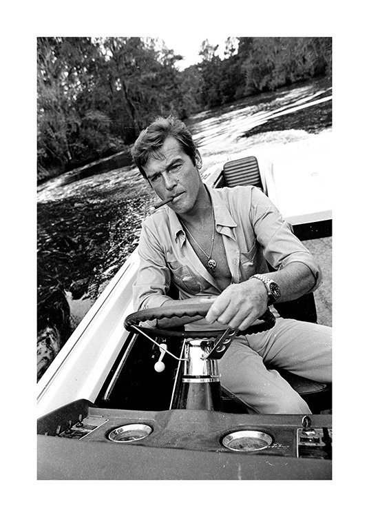 – Zwart wit foto van Roger Moore aan het roer van een motorboot met een sigaret in zijn mond