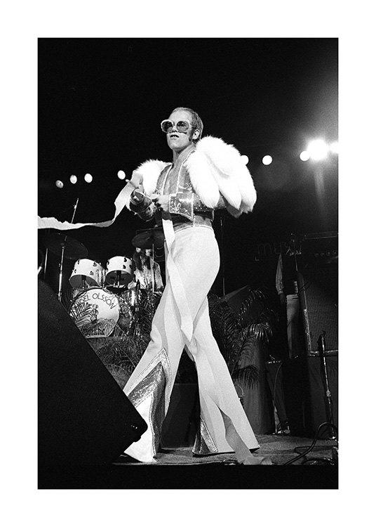  – Zwart wit foto van de zanger Elton John, in een witte jumpsuit en zonnebril op het podium