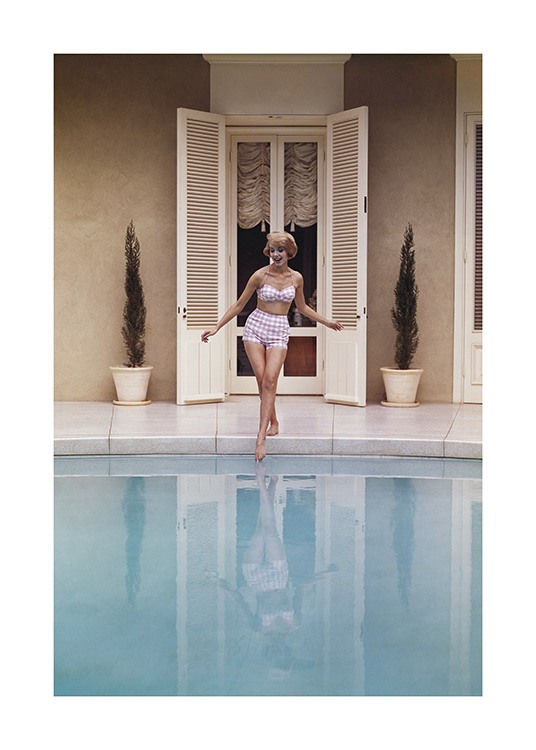  – Foto van een vrouw die haar voet in een zwembad dompelt, en een roze en witte vintage bikini draagt