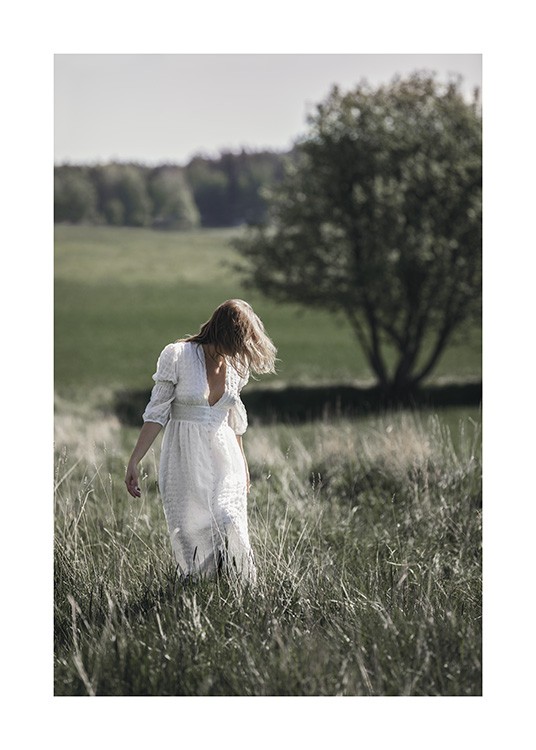  – Foto van een vrouw die een witte jurk draagt en in een veld met gras staat met bomen op de achtergrond