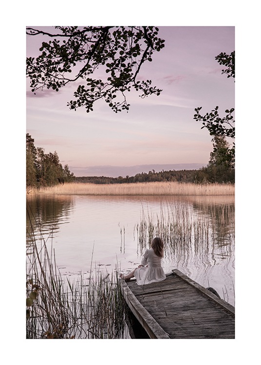  – Foto van een vrouw in een witte jurk, die op een steiger zit in een kalm meer