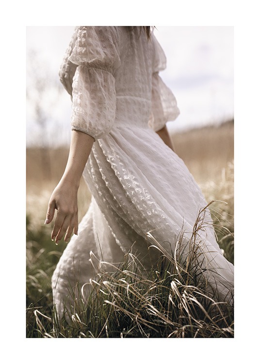  – Foto van een vrouw in een jurk in het wit, die door een veld met gras loopt