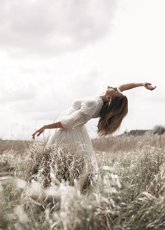  – Foto van een vrouw die op een veld met gras poseert en een witte jurk draagt