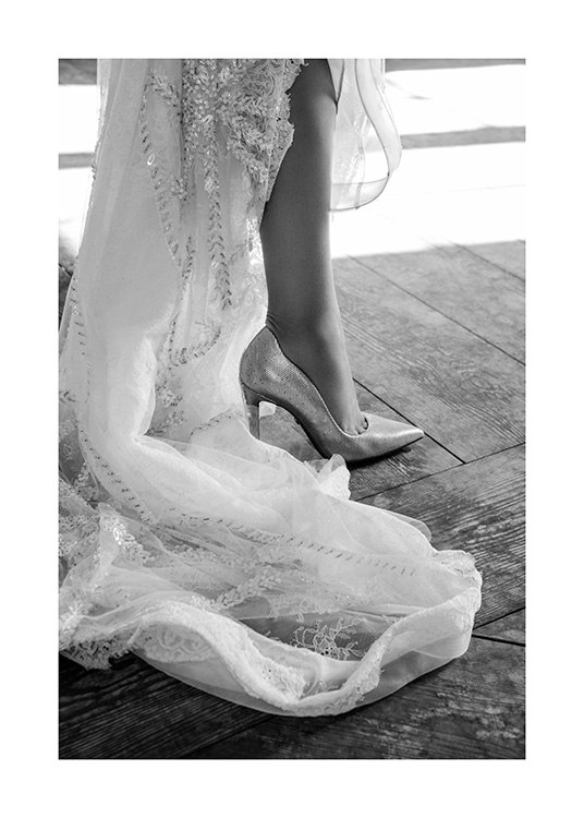  – Zwart-wit foto van het uiteinde van een witte jurk met borduurwerk en een schoen met hoge hakken