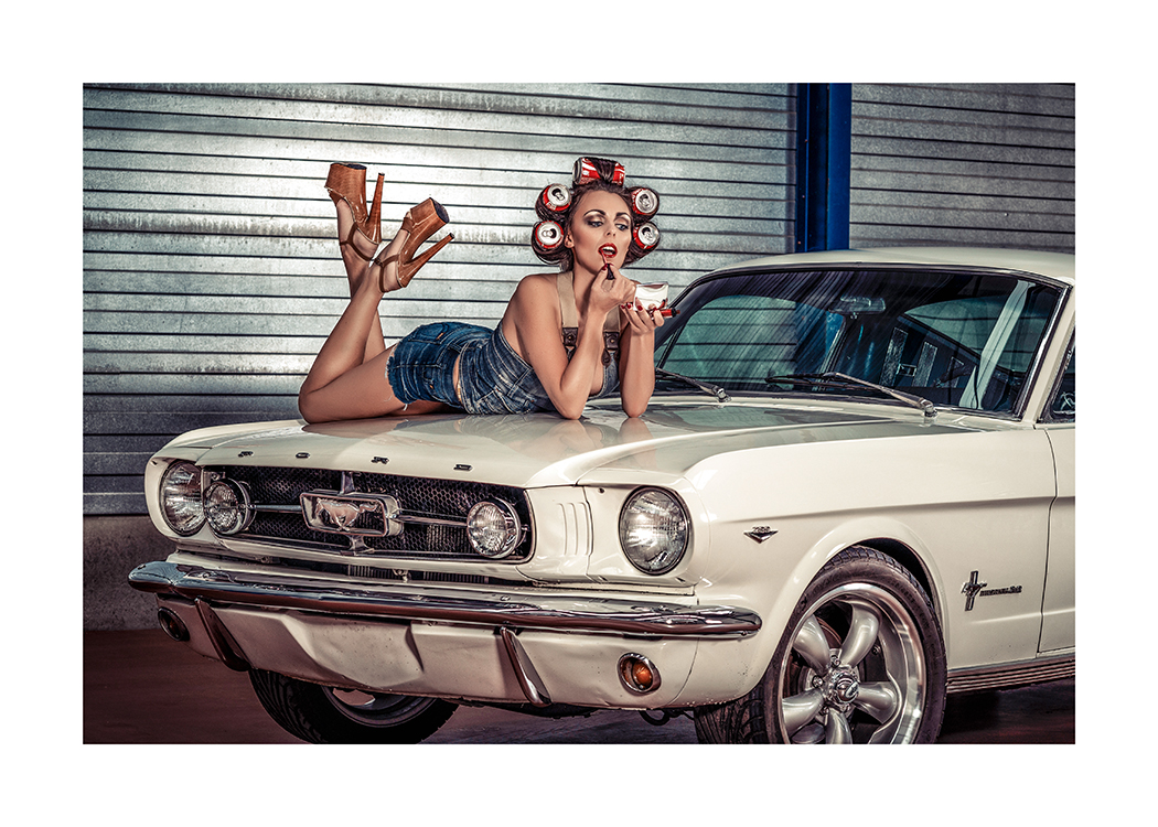  – Foto van een vrouw met limonadeblikjes in het haar, die op de motorkap van een auto ligt en haar lippen stift