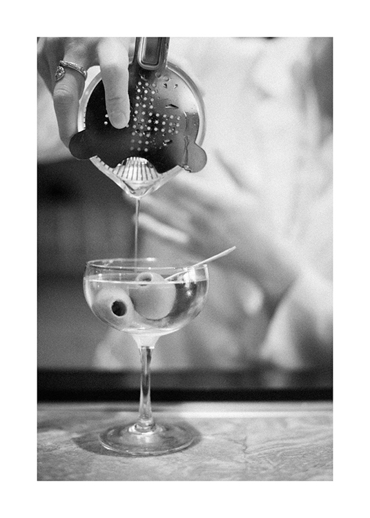 – Zwart-wit foto van een martini die wordt ingeschonken vanuit een shaker, met olijven in het glas