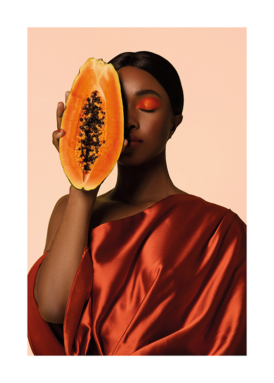  – Een vrouw in een satijnen jurk die een doorgesneden papaja voor haar gezicht houdt