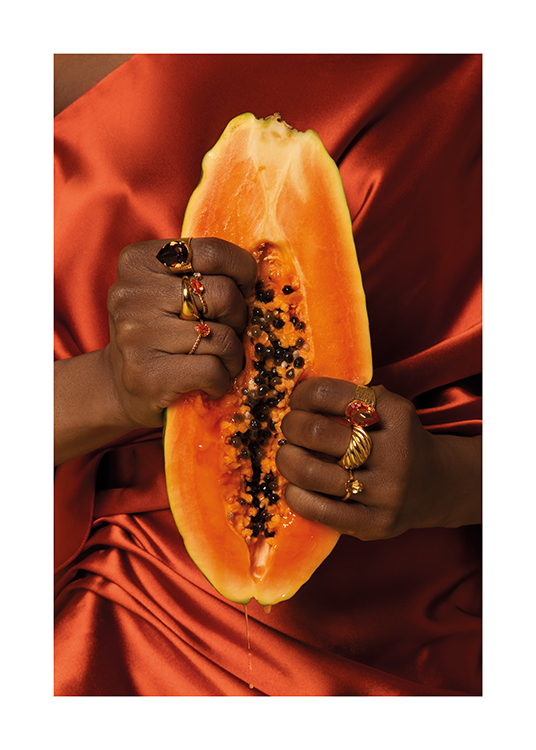  – Een vrouw in een satijnen jurk met gouden ringen die in een papajavrucht knijpt