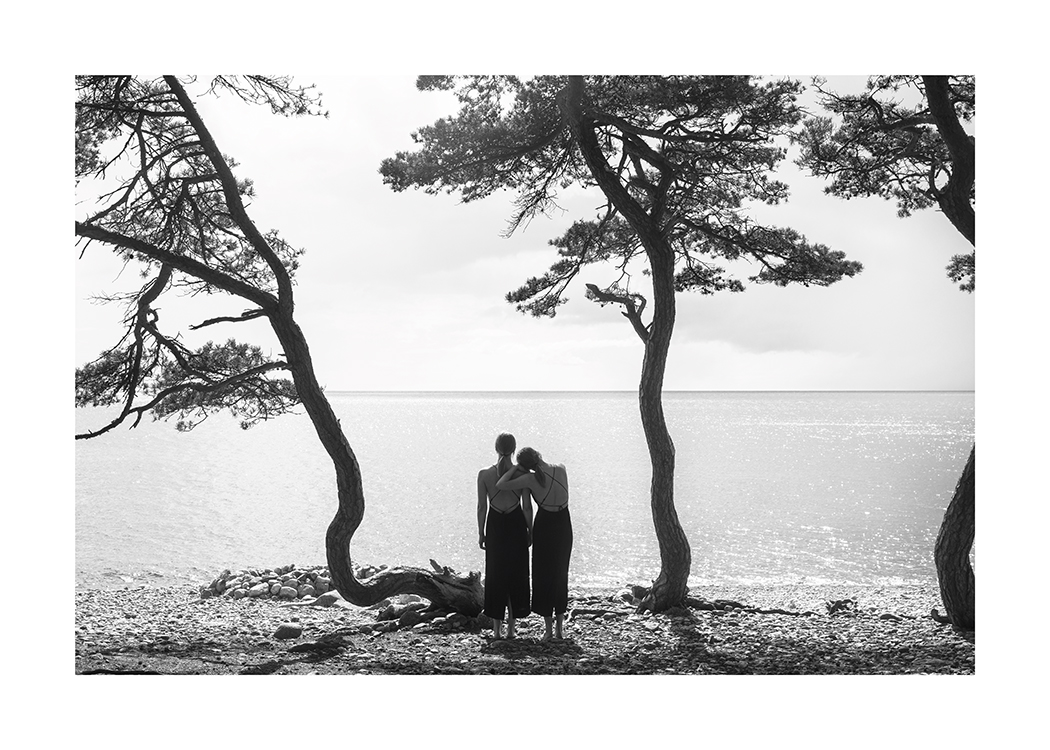  – Zwart-wit foto van een paar vrouwen die naar het water kijken vanaf een strand met bomen