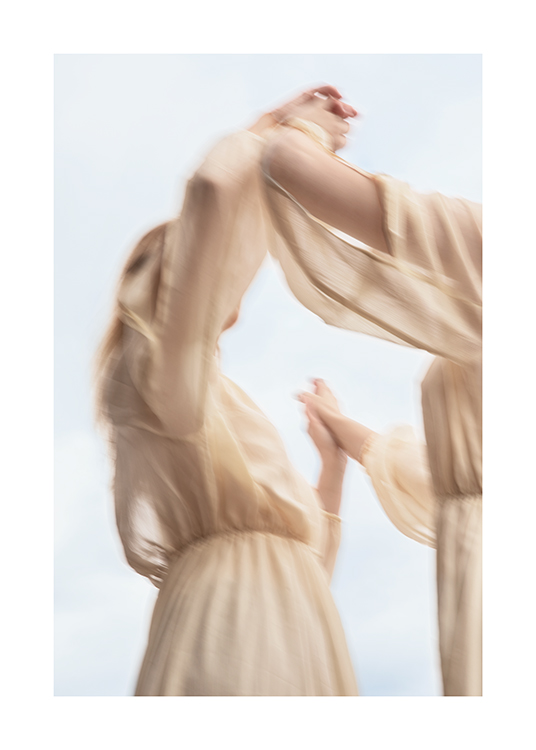  – Foto van een paar vrouwen in beige jurken die elkaars handen vasthouden, met een blauwe lucht achter zich