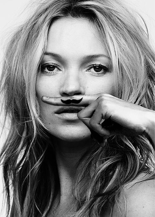  – Zwart wit foto van Kate Moss die een vinger boven haar mond houdt met daarop een snor